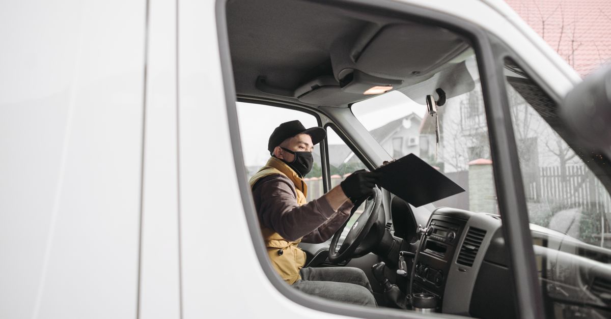 Masked delivery person inside a van holding a clipboard, illustrating modern delivery service.