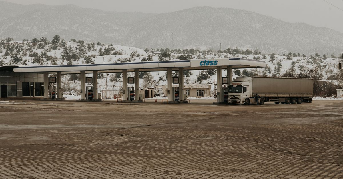 A snowy gas station with a truck and mountains in the backdrop, offering a serene winter scene.
