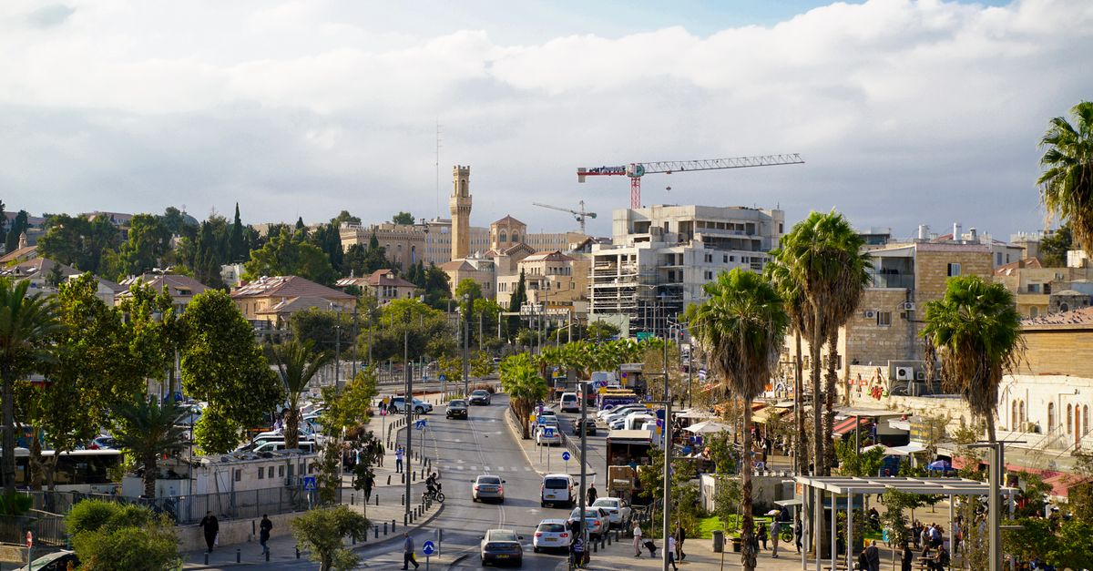 View of Jerusalem streets with historic buildings and palm trees under a clear blue sky.